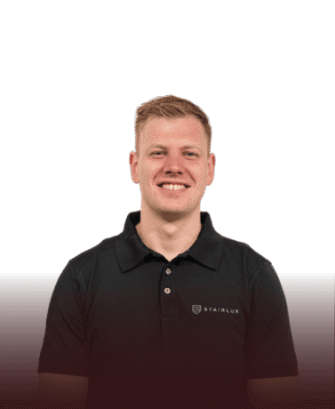 Man in zwart Stairlux uniform met logo, lachend, professionele uitstraling.